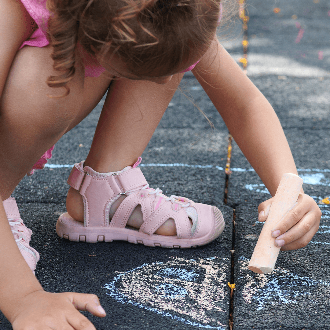 Girl drawing on the pavement with sidewalk chalk – creative outdoor activity for kids.