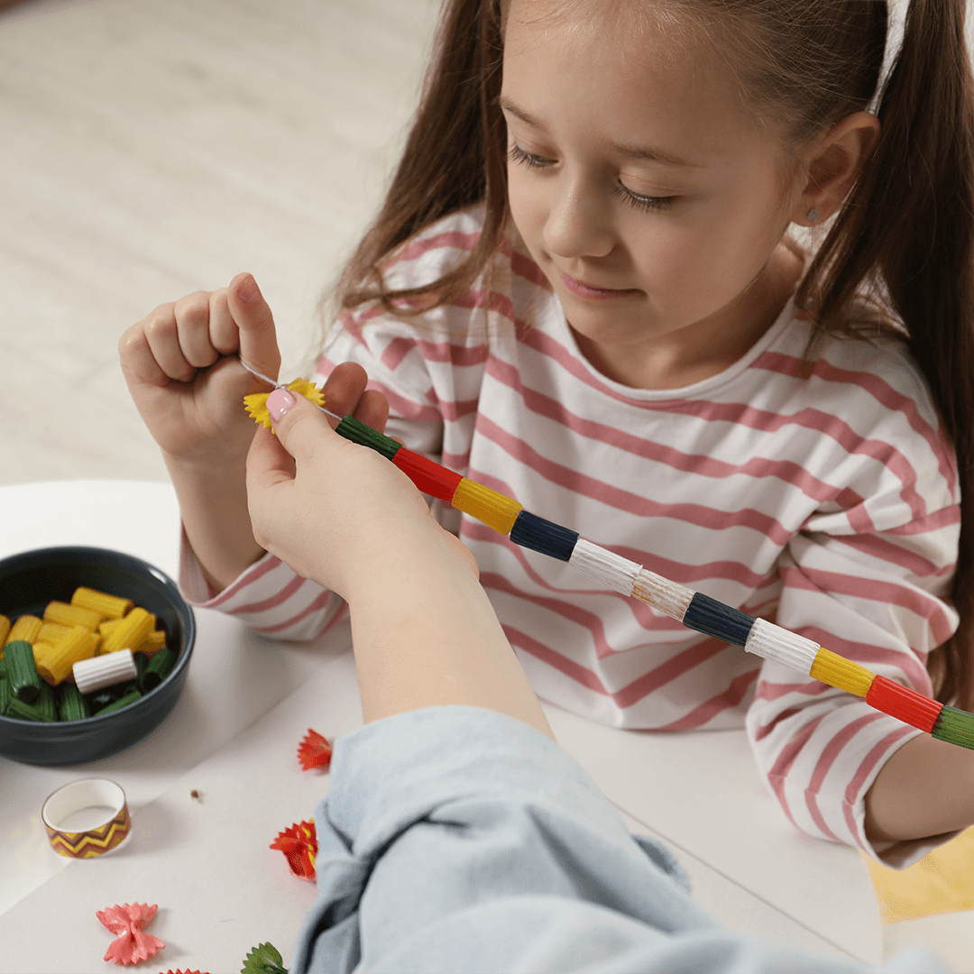A girl making a pasta necklace with her mom – creative and easy activities for kids at home.