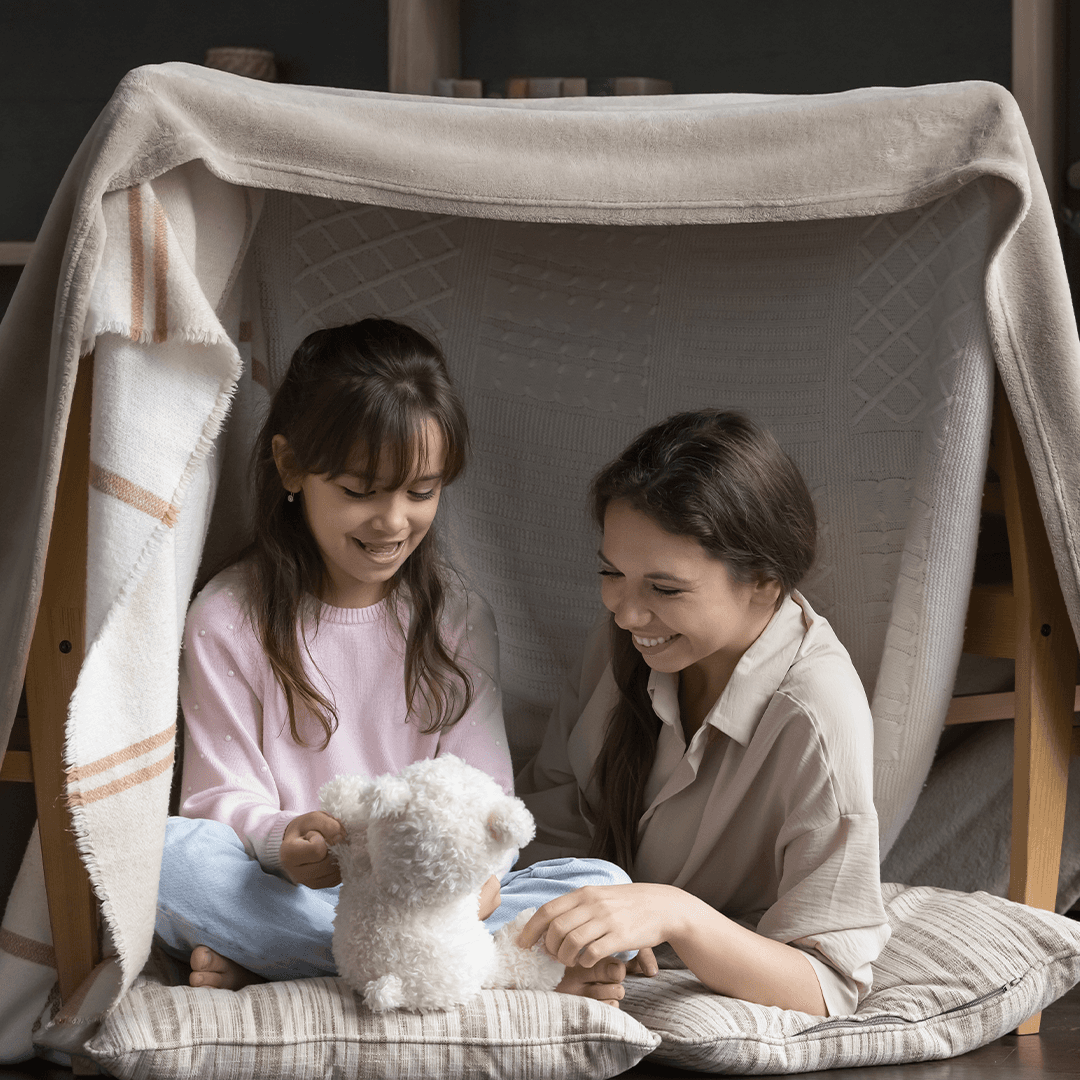 Mom and daughter playing in a blanket and chair fort – cozy indoor play idea for rainy days.