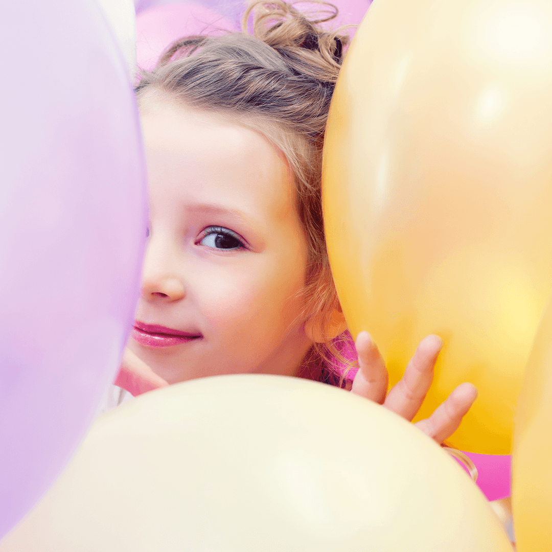 Mädchen schaut hinter Luftballons hervor – kindergeburtstag ideen voller Spaß