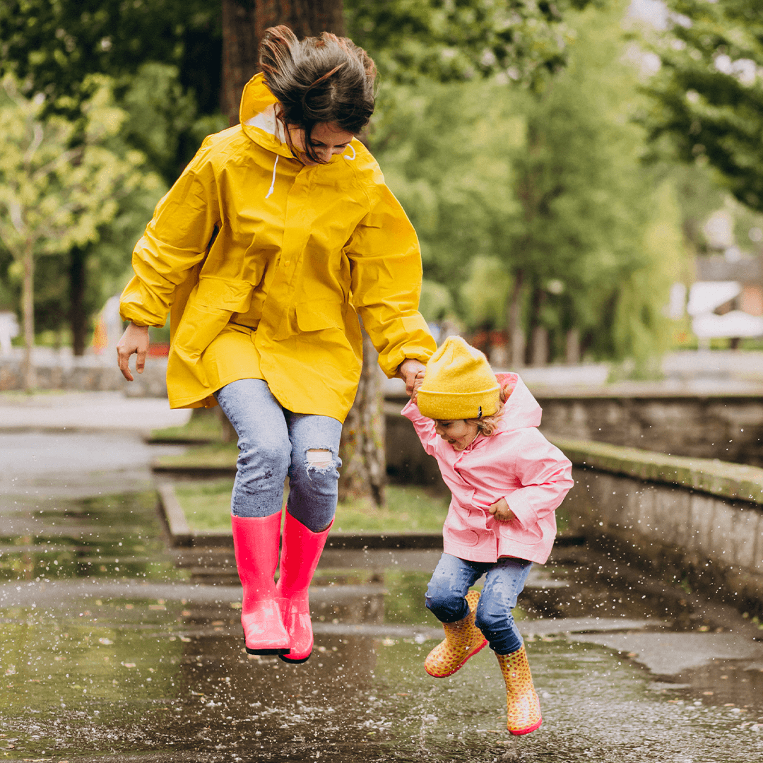 Mutter und Tochter springen in Pfützen – aktive Ideen bei Regenwetter mit Kindern.