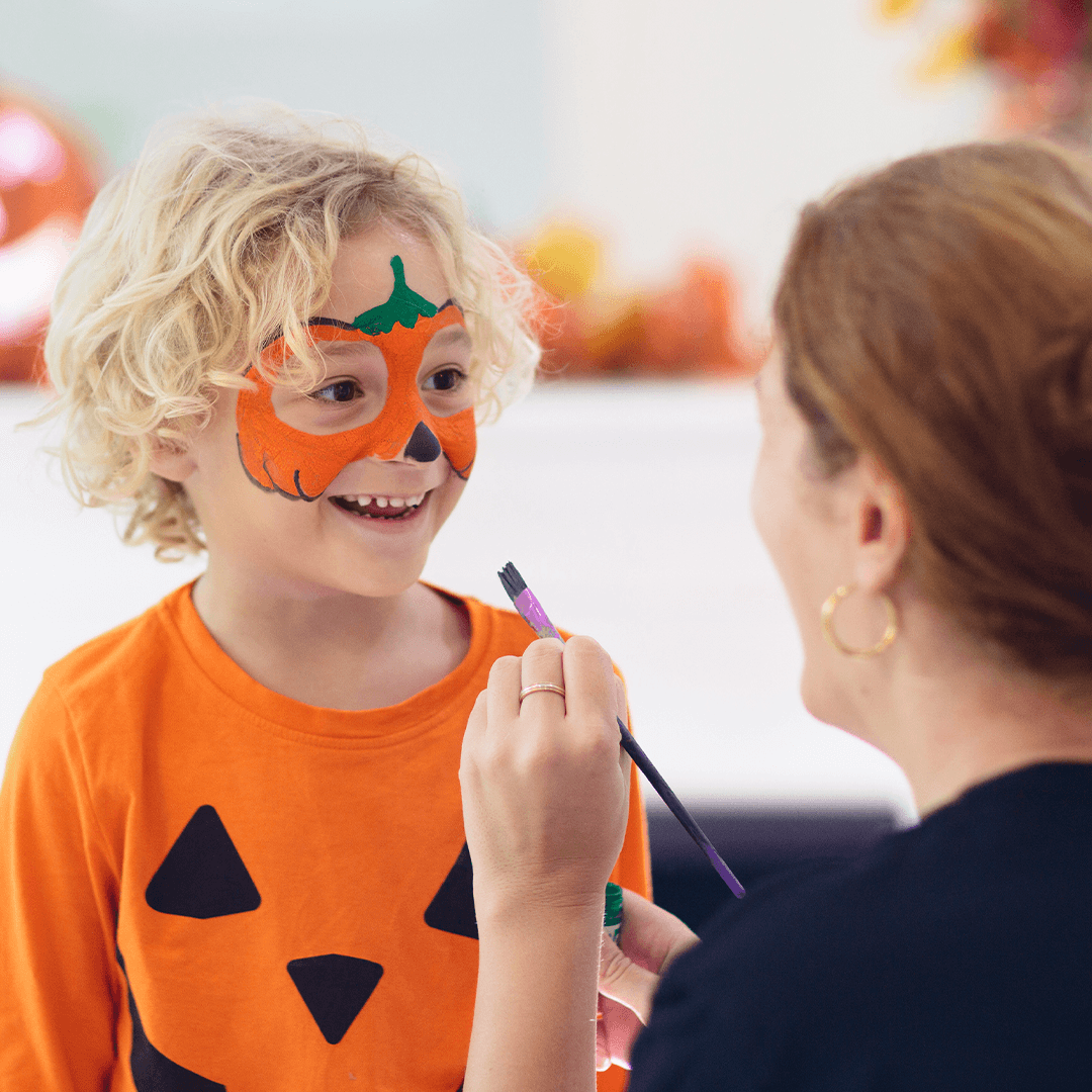 Mutter malt ihrem Sohn ein Kürbismotiv ins Gesicht zu Halloween